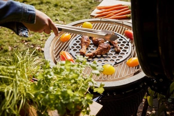 Persoana ce intoarce pulpe de pui pe gratar Original Large de la Grill Guru